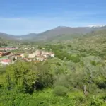 Pueblo del Valle del Jerte entre huertos y laderas verdes, con sierra nevada al fondo (Cáceres)